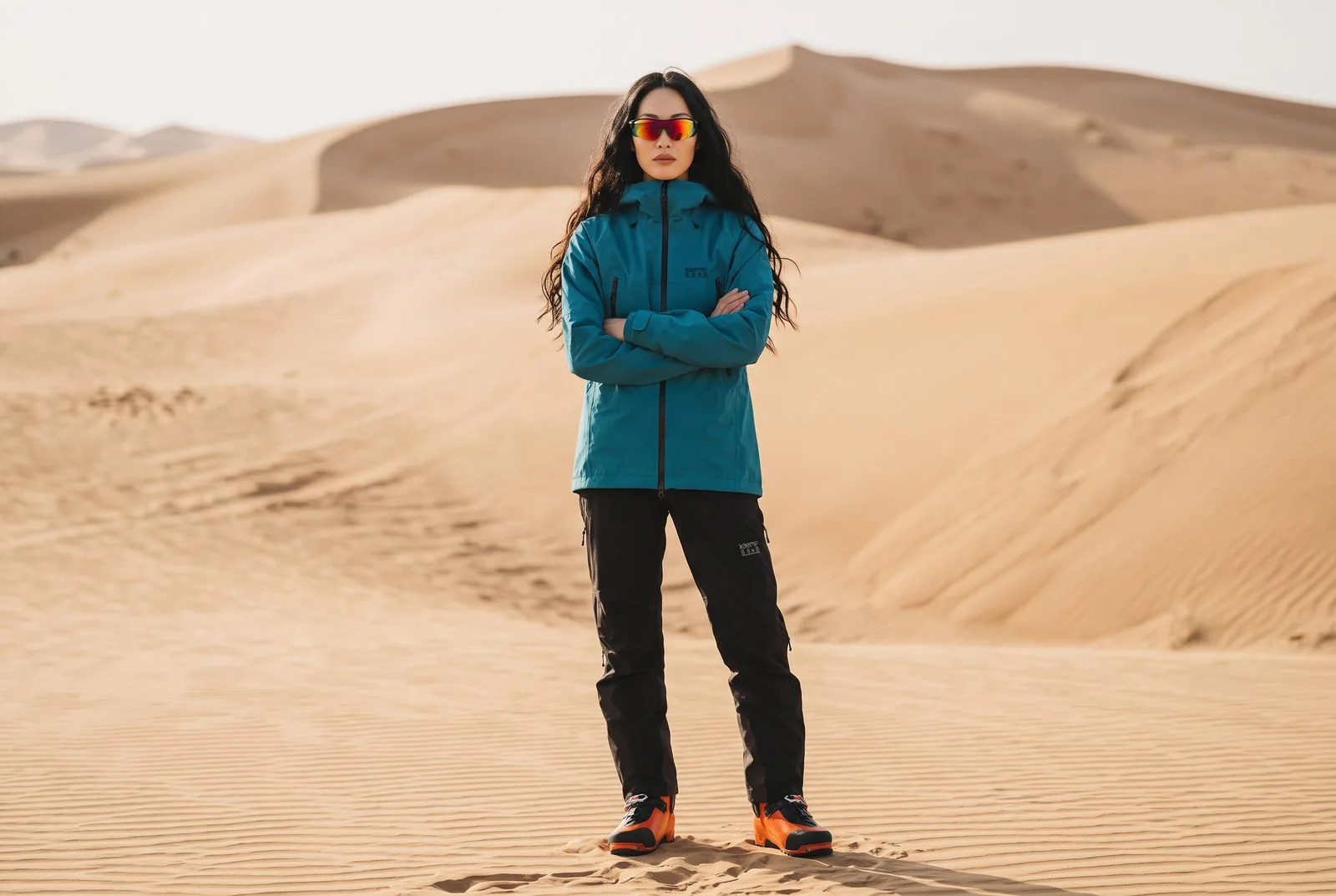 Woman in a teal KAEMP 8848 jacket and black trousers standing on desert sand dunes